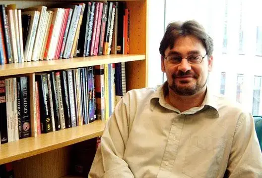 Mark Griffiths, autore e professore, seduto accanto a una libreria in un ufficio accademico